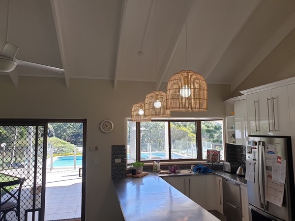 A kitchen with woven pendant lights and a pool through the window