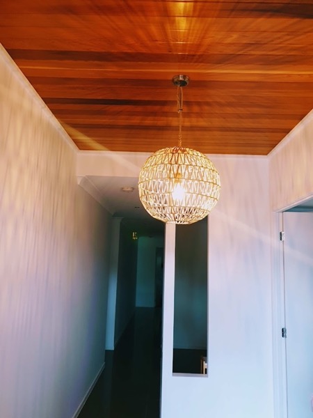 A woven pendant light below a timber-lined ceiling